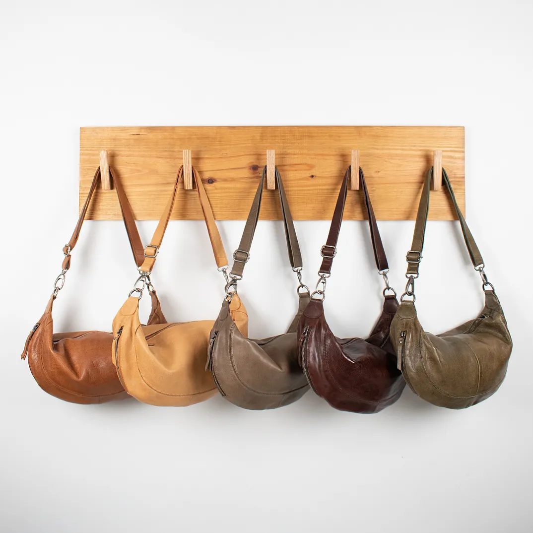 Latico leather sling bags hanging from a wooden rack, from the Latico home page.