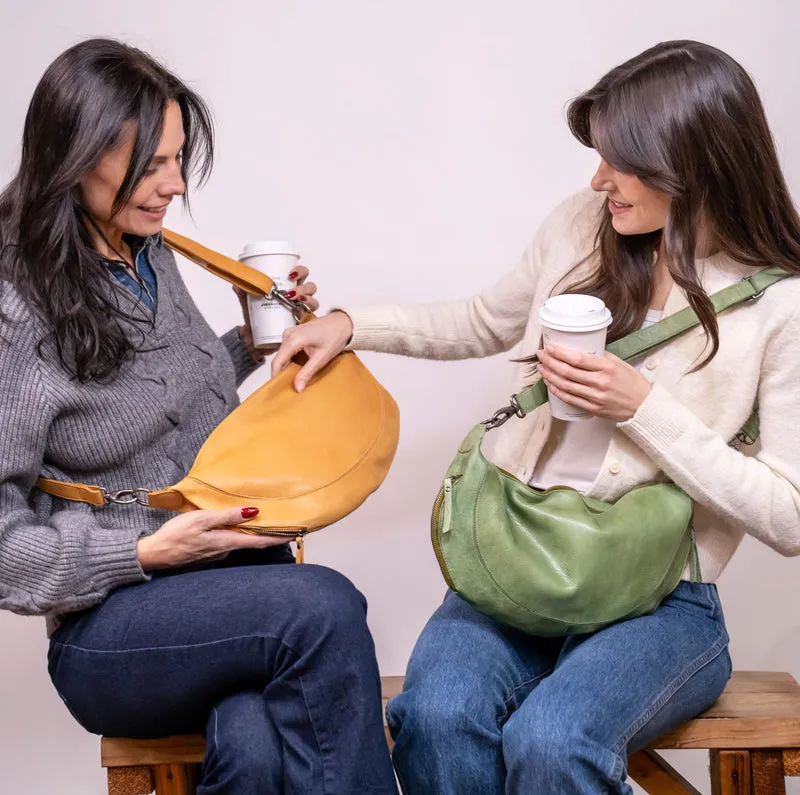 Two women sitting on stools holding handbags and coffee cups.