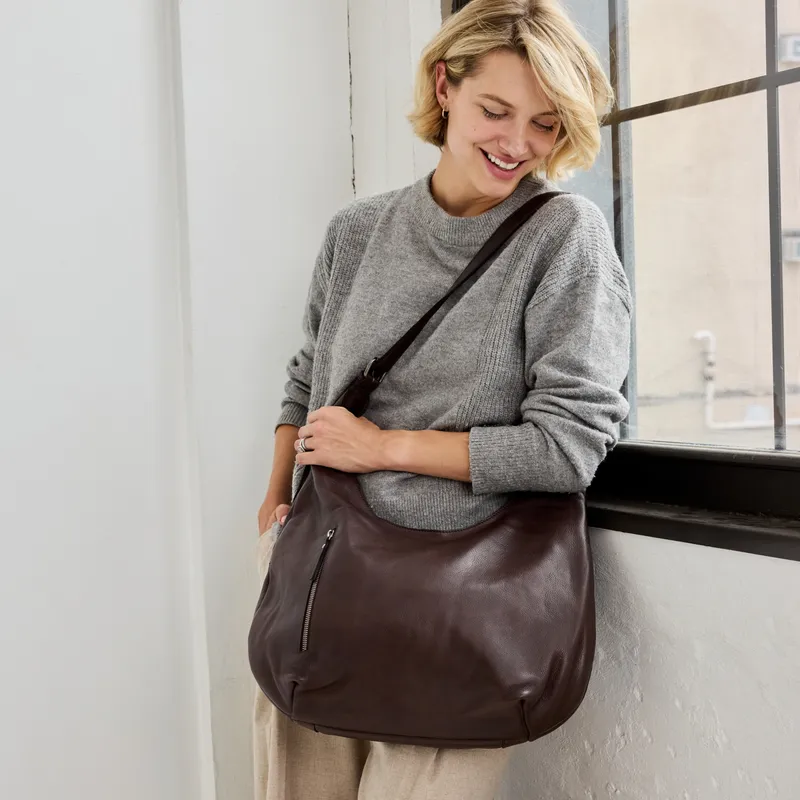A woman wears the Beacon Stain-Washed Leather Shoulder Bag in brown, from the Beacon product page.